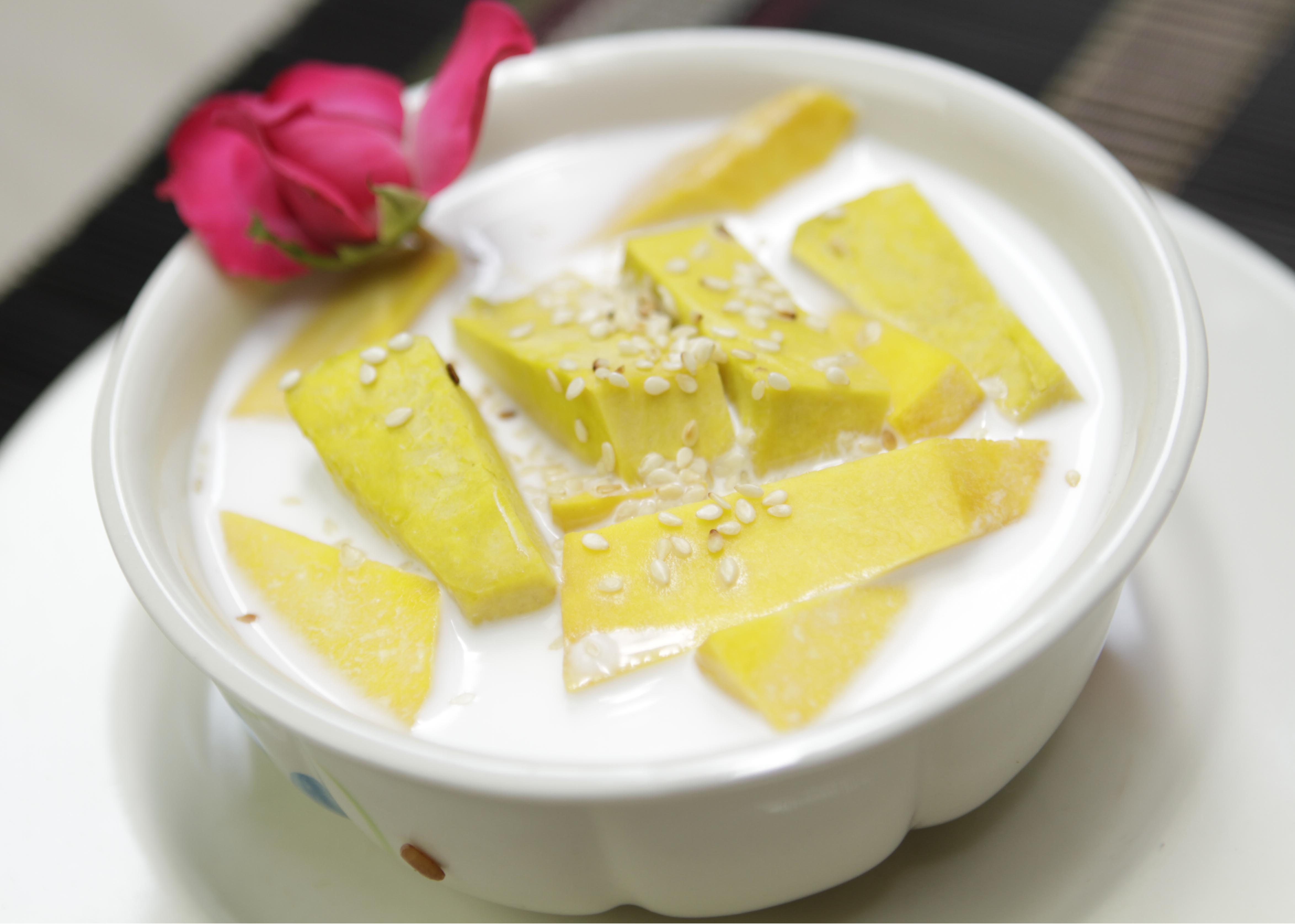 Steamed pumpkin slices in sweet coconut milk dessert, topped with sesame seeds and a pink rose as garnish.