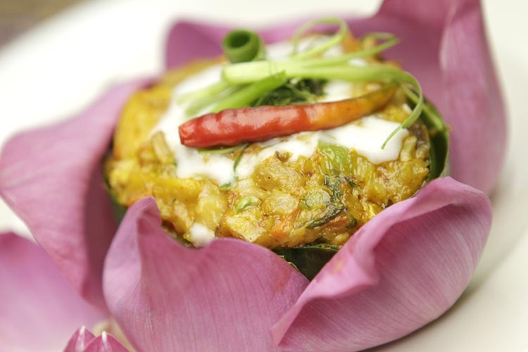 Hamok Isaan curry in a banana leaf bowl with lotus flowers placed around it.