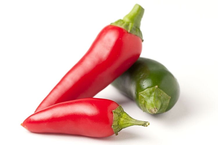 Fresh red and green chili peppers on a small white plate.