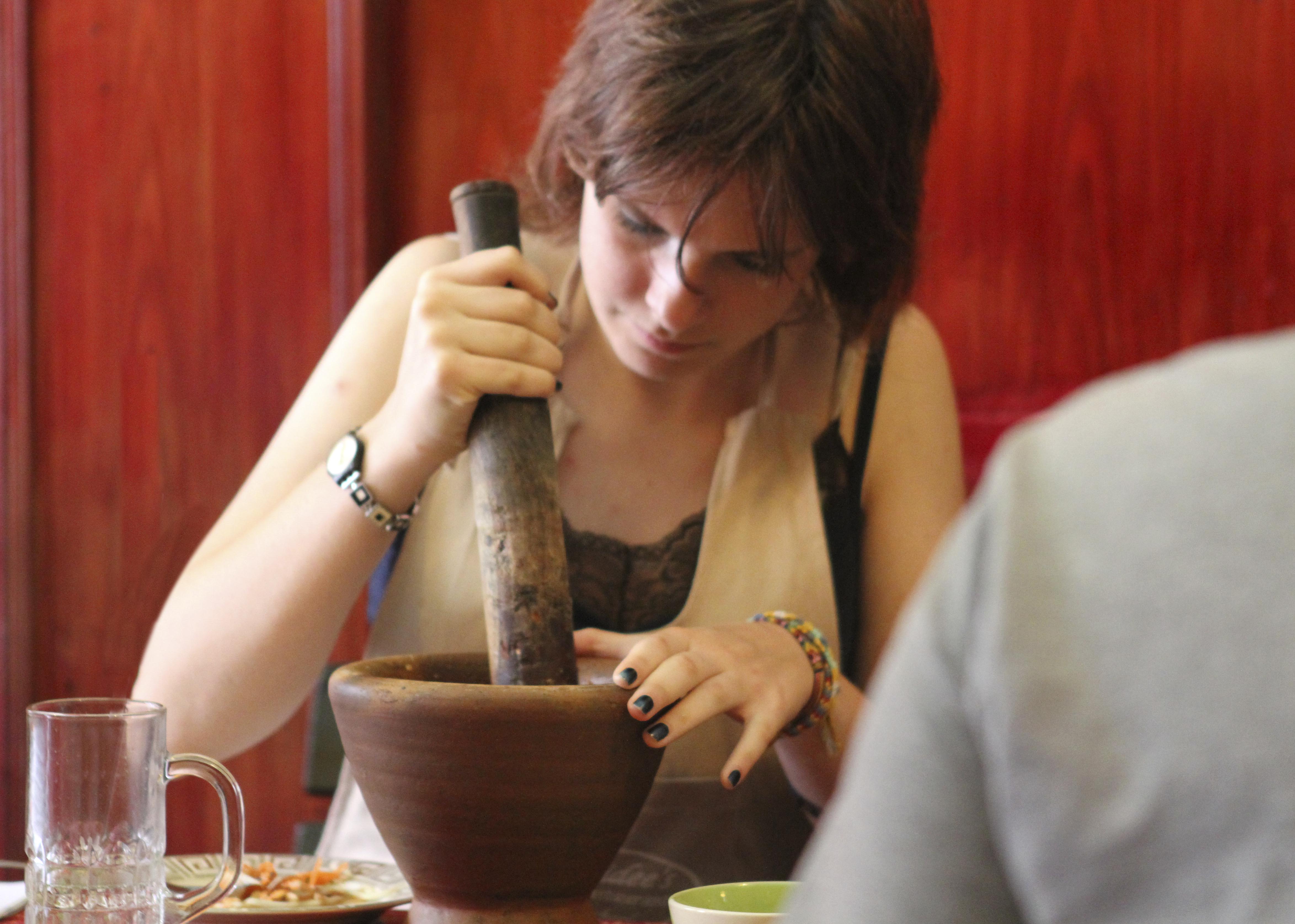 Cooking class student making chili paste with a mortar and pestle.