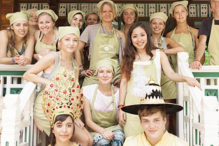 Group of cooking class students wearing aprons and headscarves, giving the traditional Wai with hands pressed together