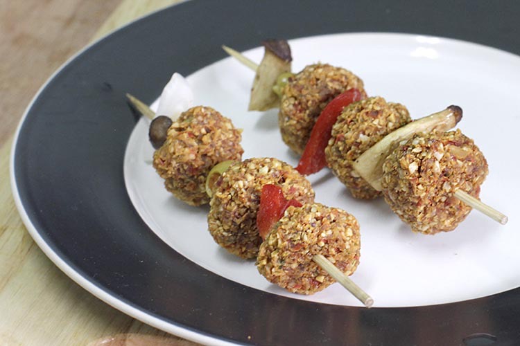 Raw vegan vegetable Kebabs made from nut and seed paste, placed on wooden stick between olives, mushroom and red pepper slices.