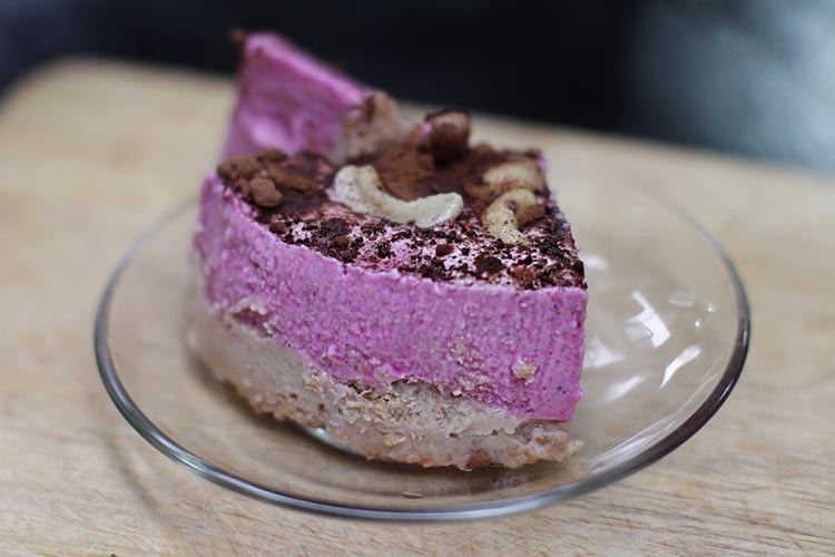 Raw dragon fruit ice cream cake made with red (magenta) dragon fruit, a cashew nut paste base, topped with grated raw cacao powder and cashew halves.