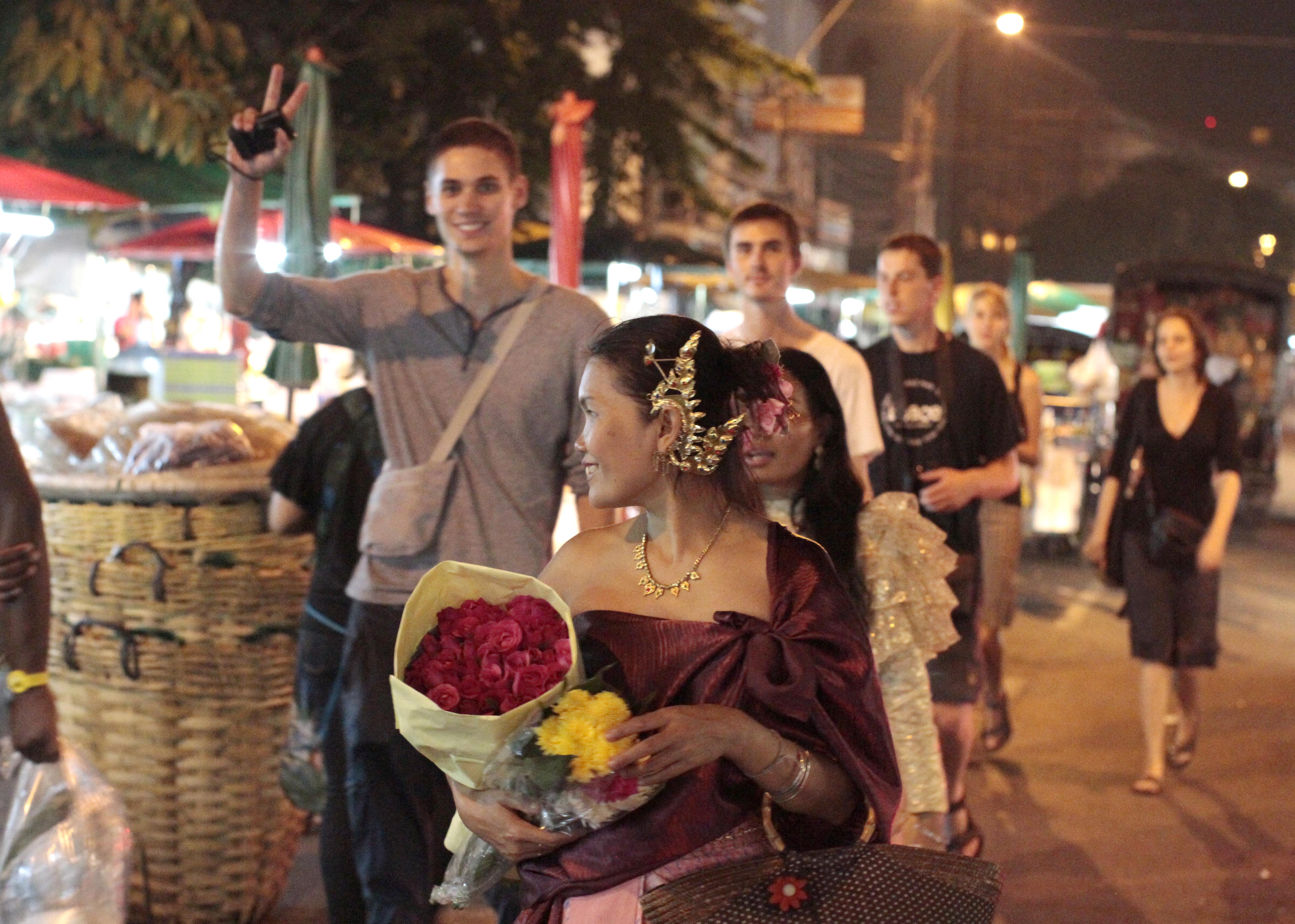 Singles and Lovers party students walking through the Bangkok flower market with the lead student holding a bouquet of roses.