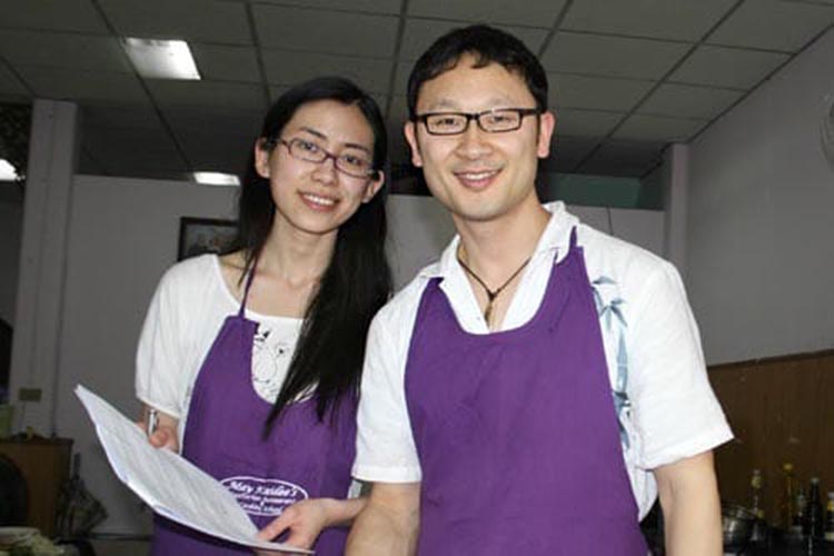 Student couple wearing aprons taking a break from cooking. Woman holding class notes and both are smiling.
