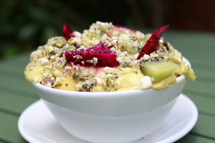 Fruit salad with mango sauce. Slices of dragonfruit, kiwi and water apple topped with mango sauce and nuts in a white ceramic bowl.
