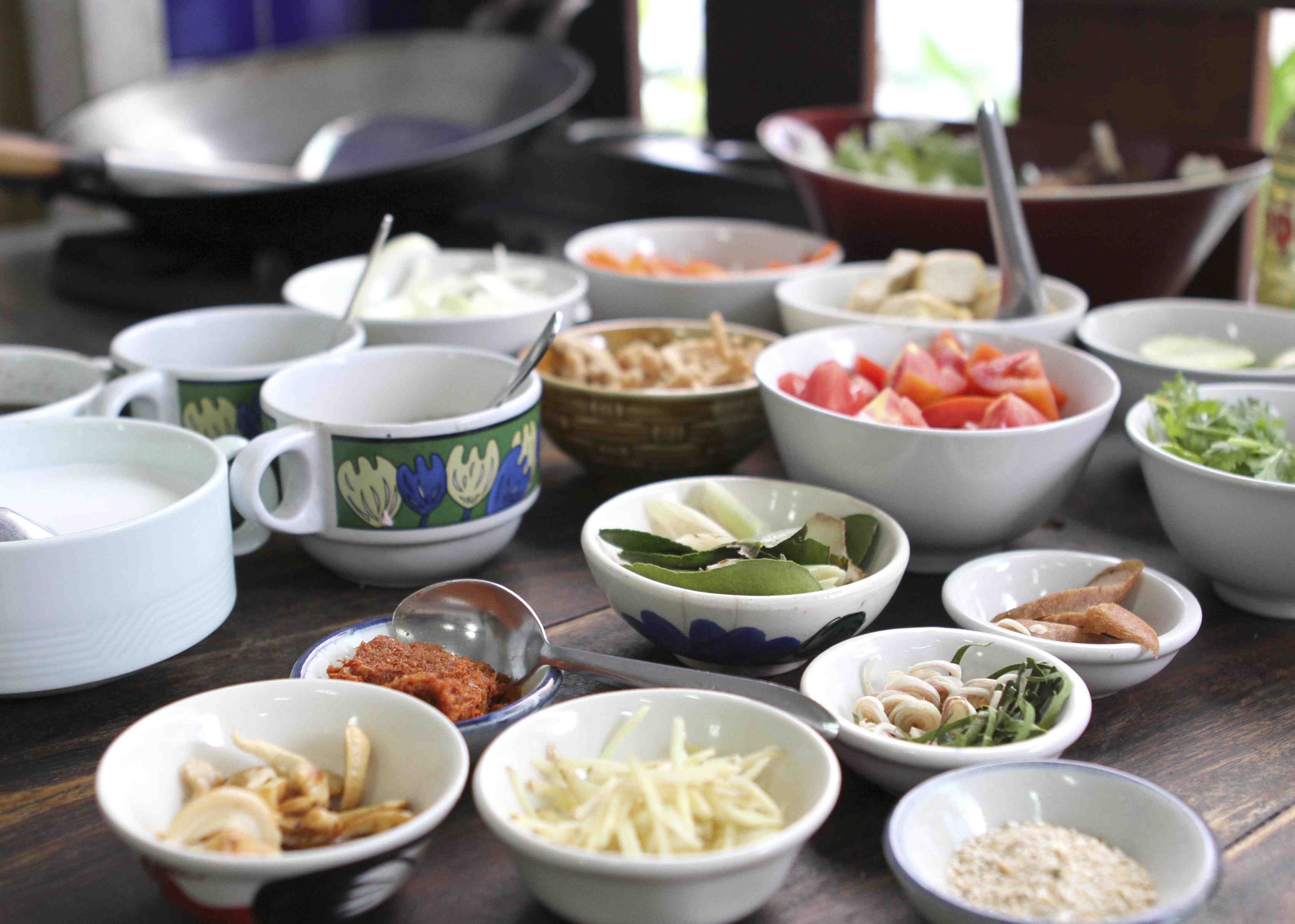 Ceramic bowls of Thai ingredients on a rustic wood table.