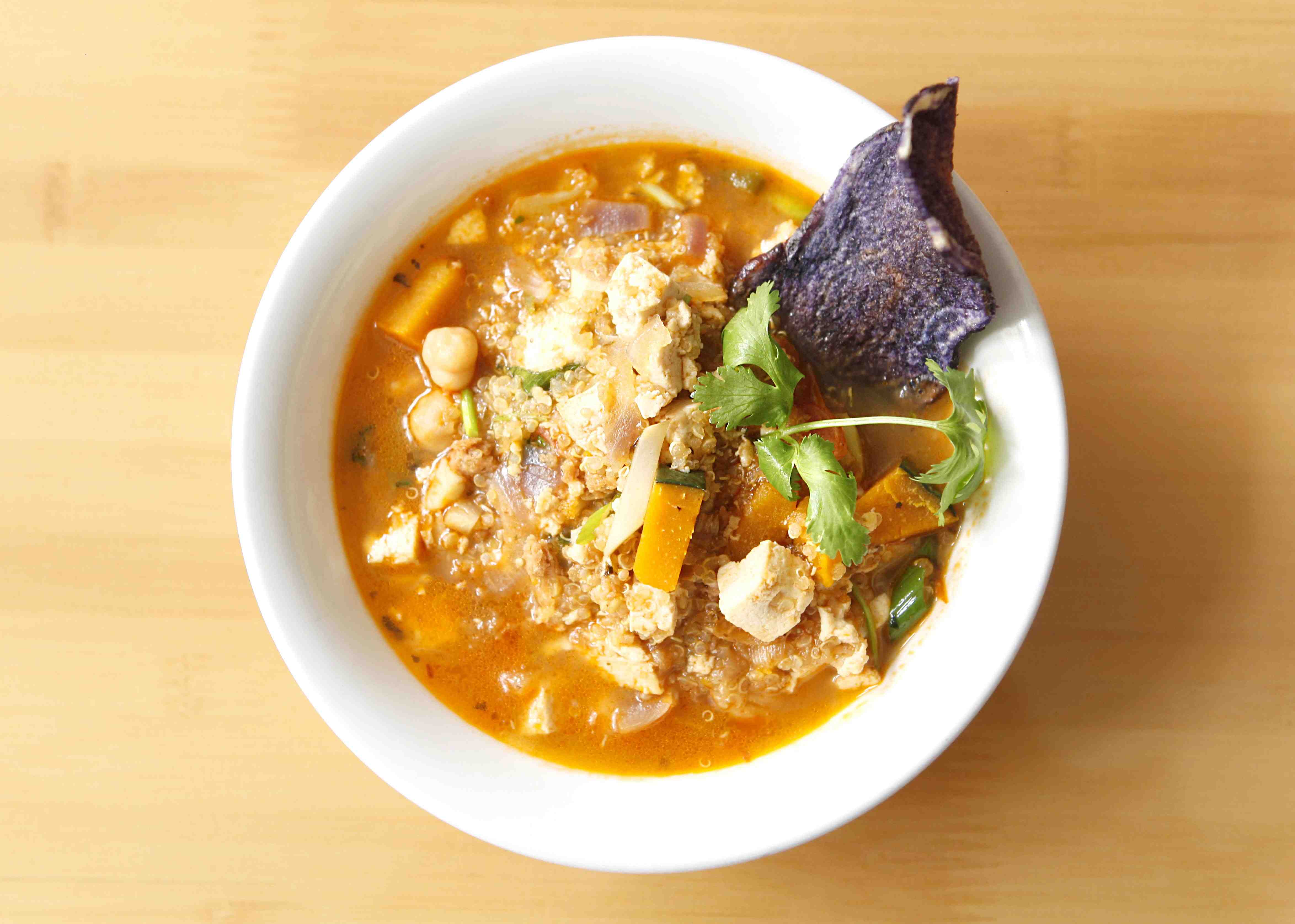 Quinoa stew in a white bowl with a beet root chip.