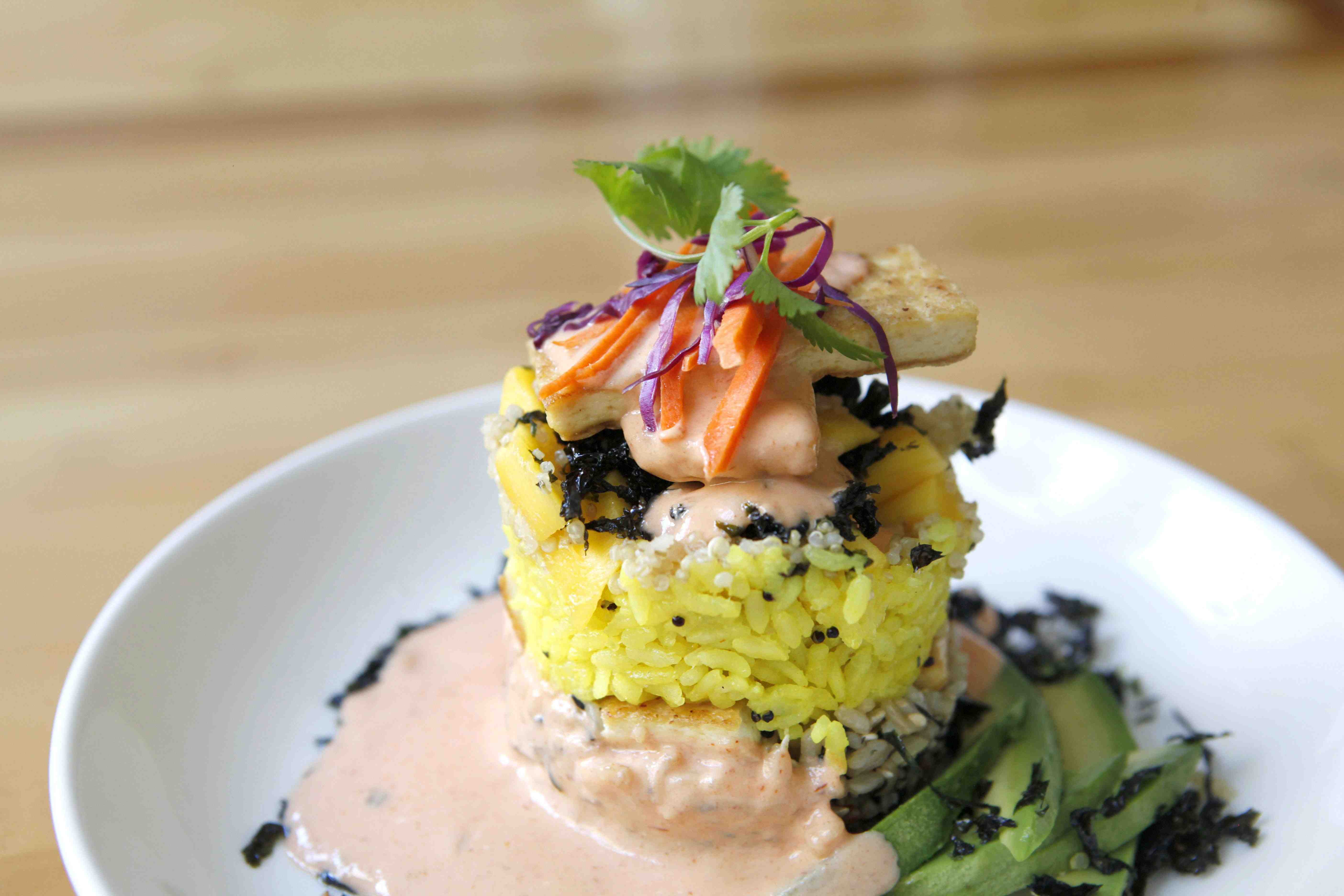 Turmeric Rice, served as a decorative cylindrical shape topped with tofu slices, thin carrot and cabbage slices, avocado slices and sprinkles of dried seaweed with a tofu cream sauce.