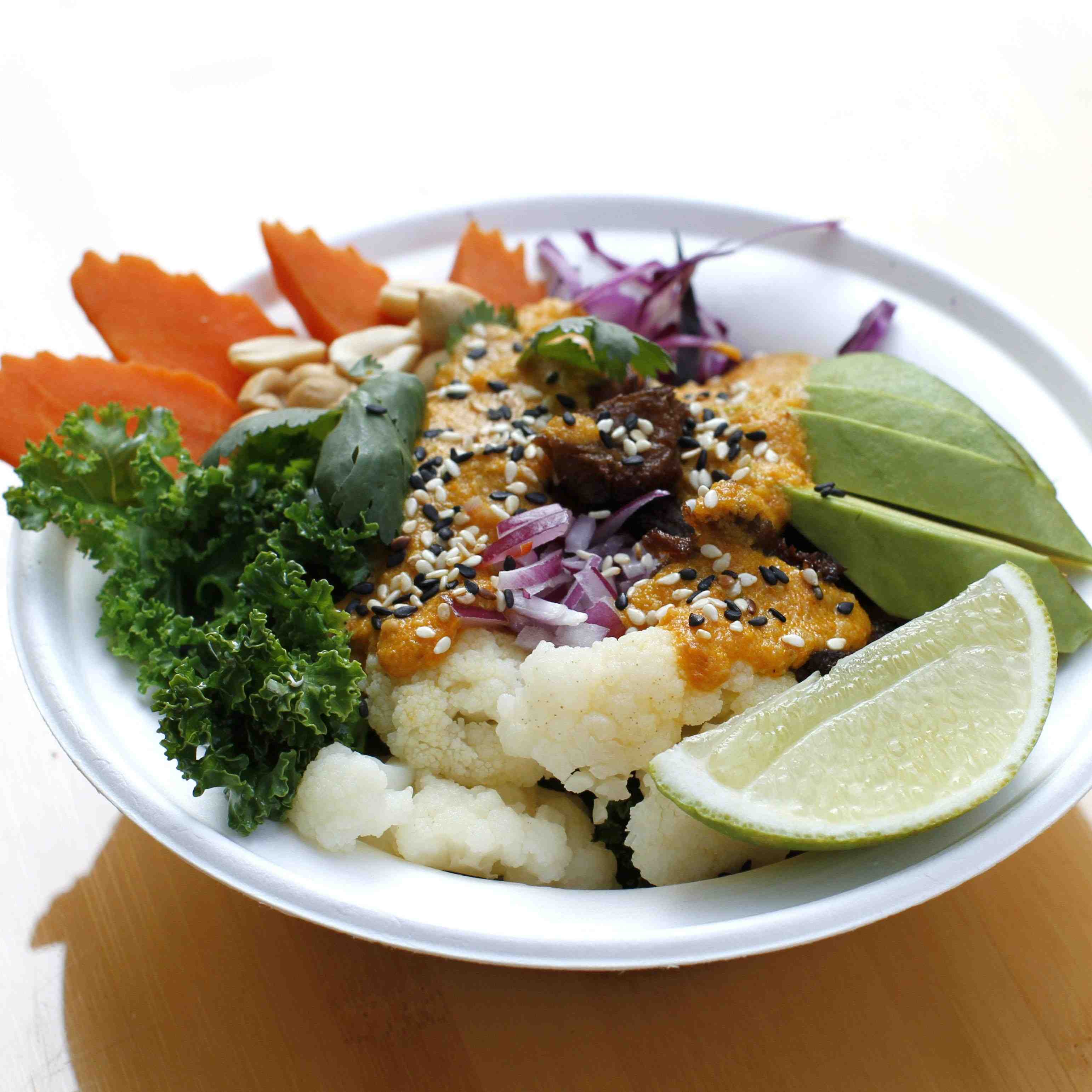 Veg Bowl, a combination of raw and steamed vegetables, carrot, cauliflower, red cabbage, avocado with tangy dressing and a slice of lime.